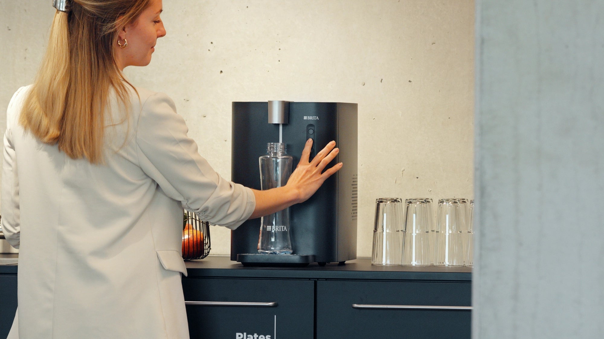 Person filling a reusable bottle at a BRITA Water Dispenser in an office kitchen.