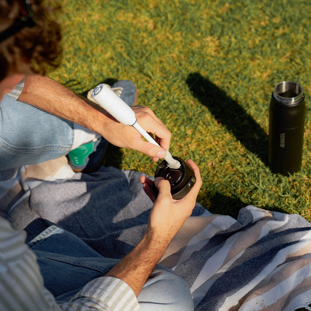 A person sitting on grass outdoors inserting BRITA LARQ filter straw in BRITA LARQ cap.
