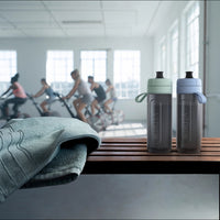 Two BRITA water filter bottles Model Active and a towel on a bench with people exercising in the background