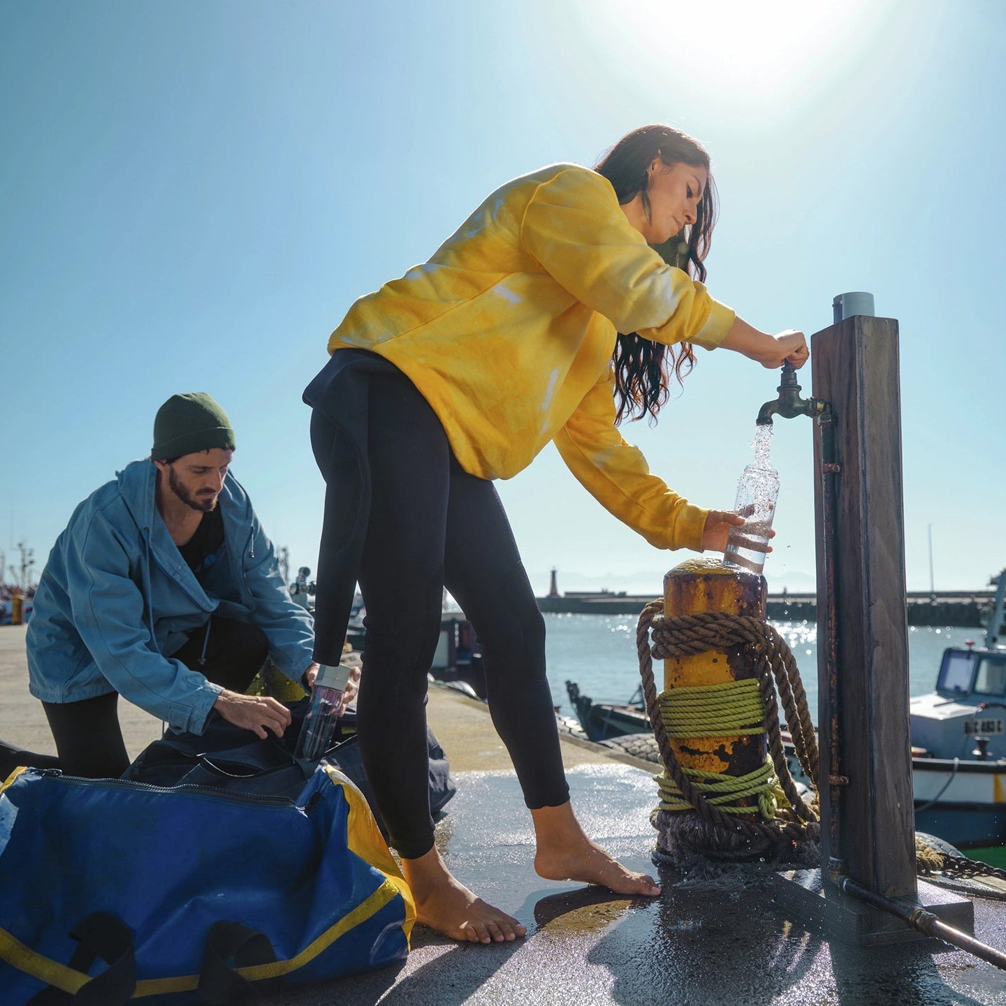 Two people on a dock by a body of water, one person is using a water faucet to fill BRITA water filter bottle Model Vital.
