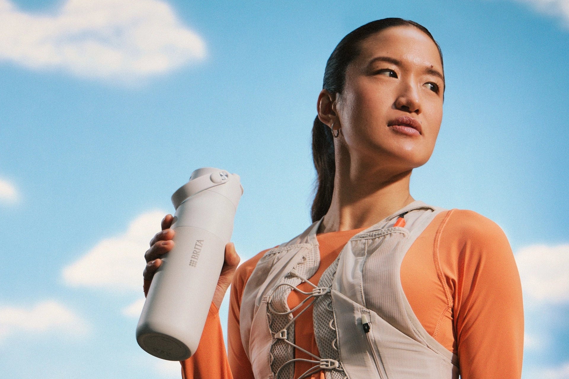 Person holding a BRITA LARQ water bottle against a blue sky background.