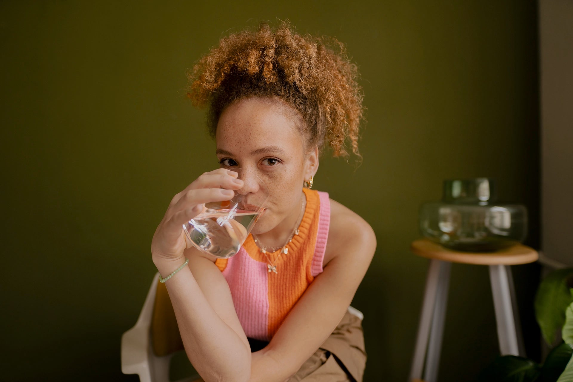 Person drinking water from a glass while seated indoors.