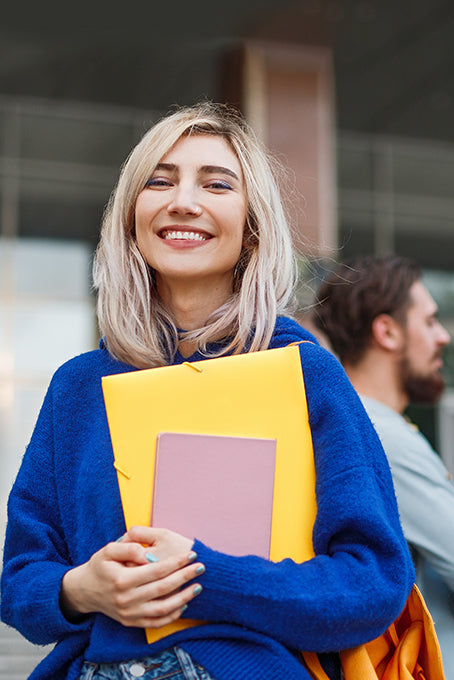 Person carrying a notebook and documents outdoors near a building entrance.