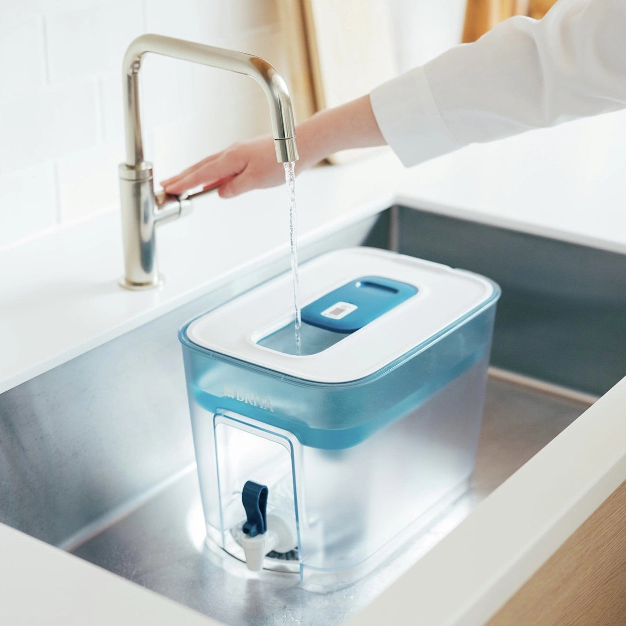 BRITA Flow water filter container being filled with water in a kitchen sink beneath a running tap.