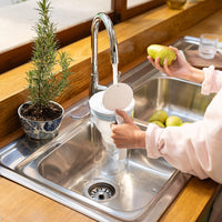 Person filling a BRITA Glass Jug with tap water at a kitchen sink.