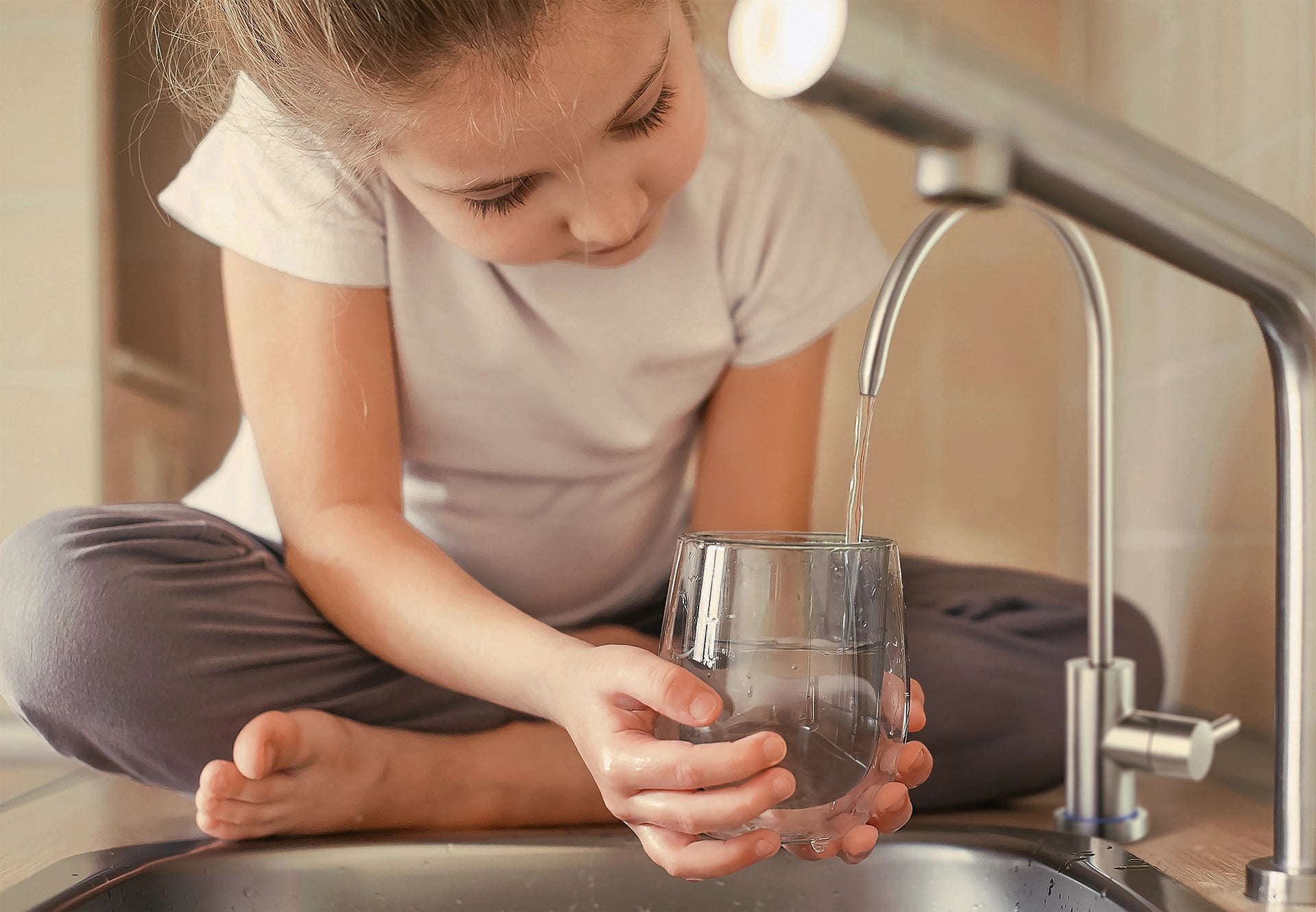 Child filling a drinking glass with filtered water from a BRITA mypure RO.