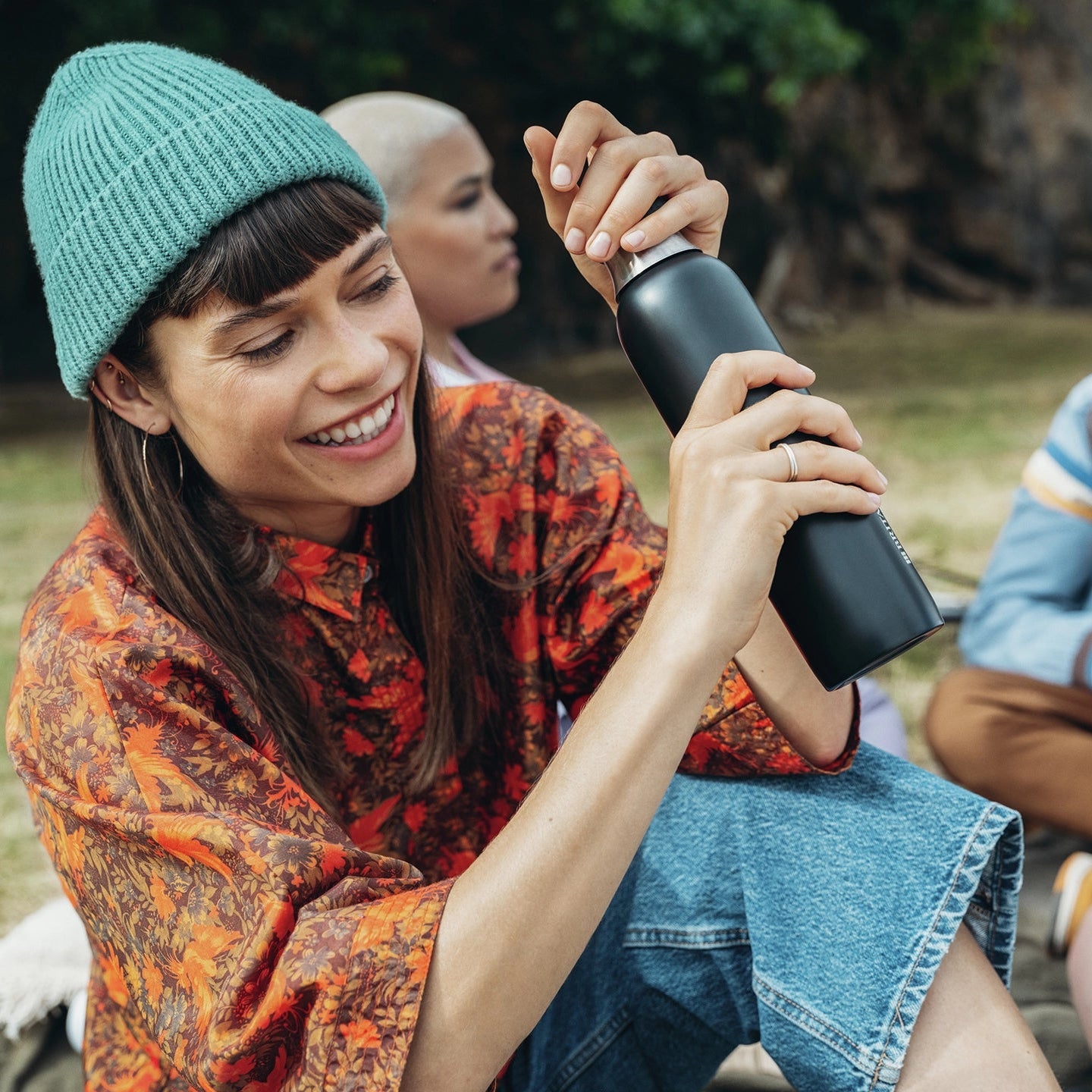 Woman in a green beanie holding a sodaTRIO Stainless Steel Bottle in black in an outdoor setting.