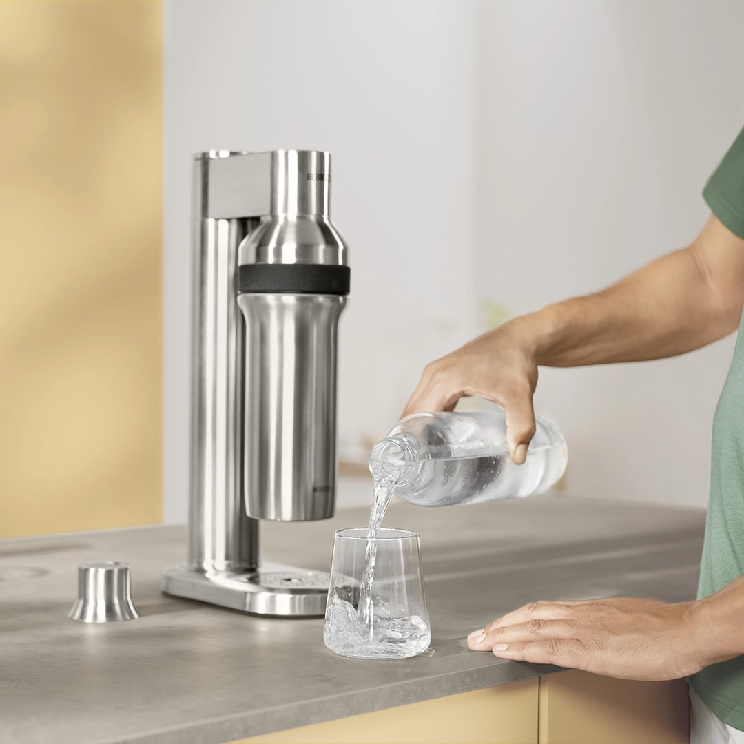 Sparkling water being poured from a BRITA sodaTRIO bottle into a drinking glass