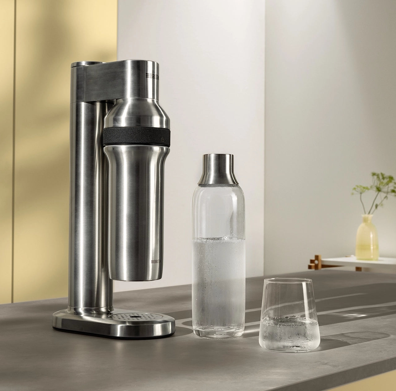 BRITA sodaTRIO Pro Sparkling Water Maker with a BRITA sodaTRIO Glass Bottle and a glass of sparkling water on a countertop.