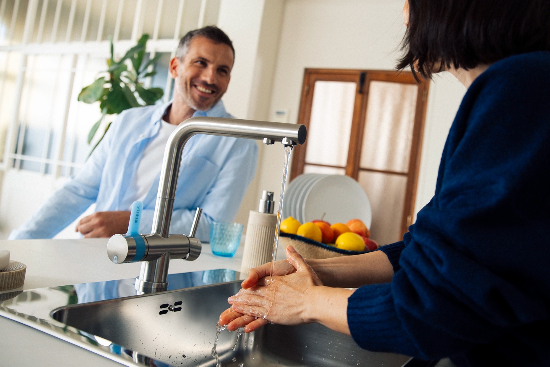 Person washing hands at a kitchen sink with a BRITA 3-way-tap while another person stands nearby.